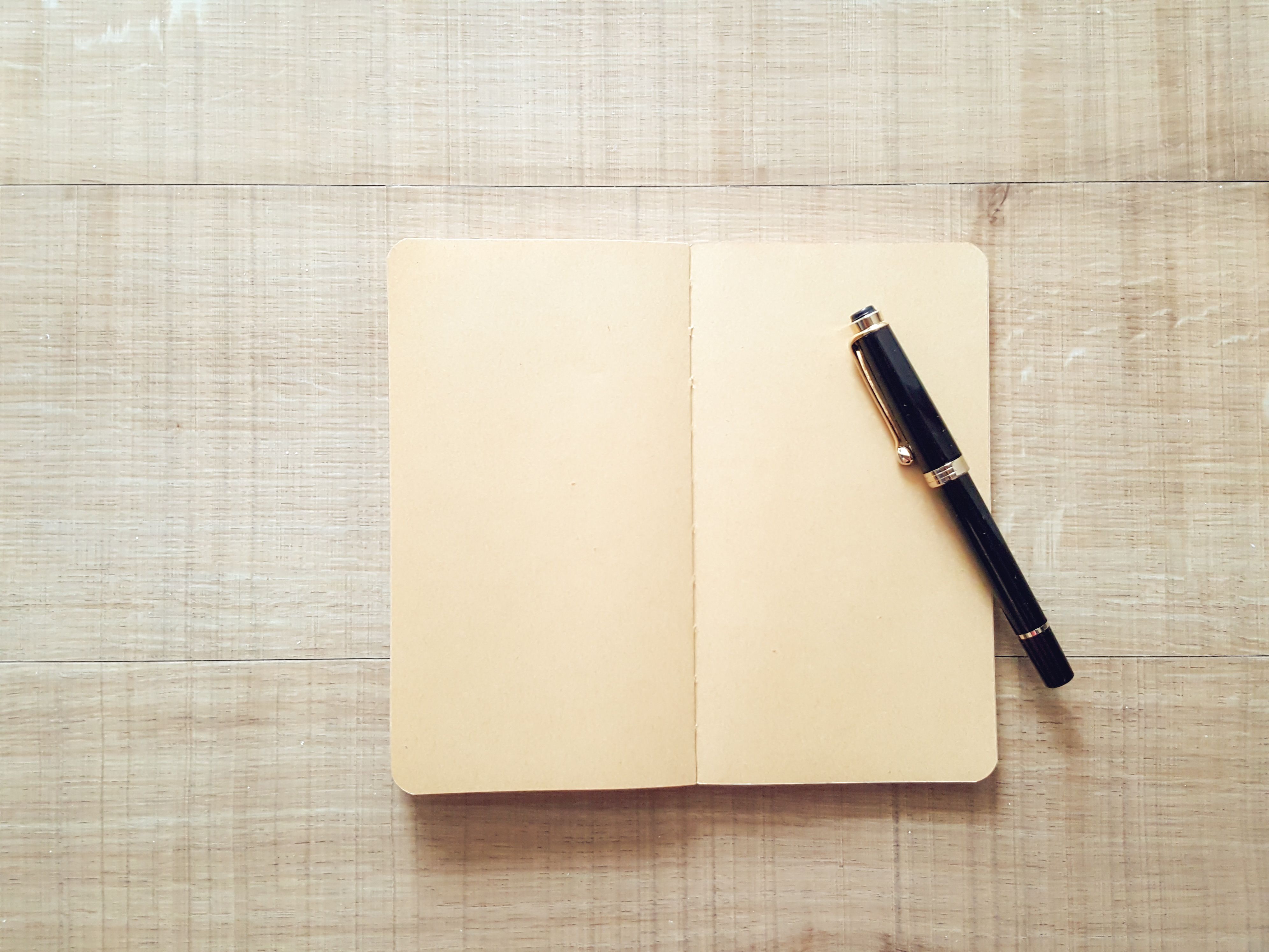 Illustrative stock photograph: Blank open notebook with a black-and-gold pen on a light wooden surface.